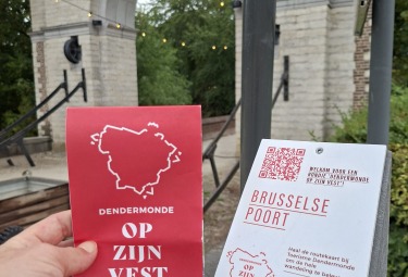 Foto met op de voorgrond de wandelkaart 'Dendermonde op zijn vest' en op de achtergrond een stadspoort