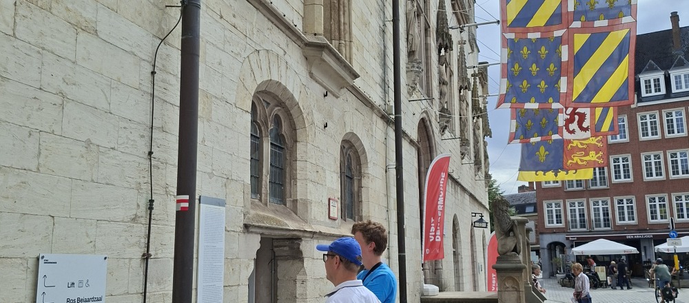 Twee mensen lezen een infobord bij de lakenhalle en het stadhuis van Dendermonde